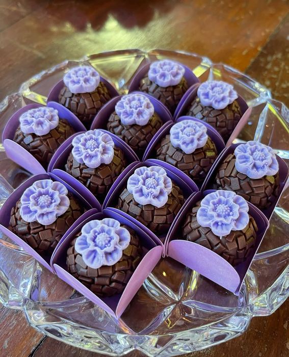 Brigadeiros com flor lilás modelada à mão, em forminhas roxas sobre bandeja de cristal