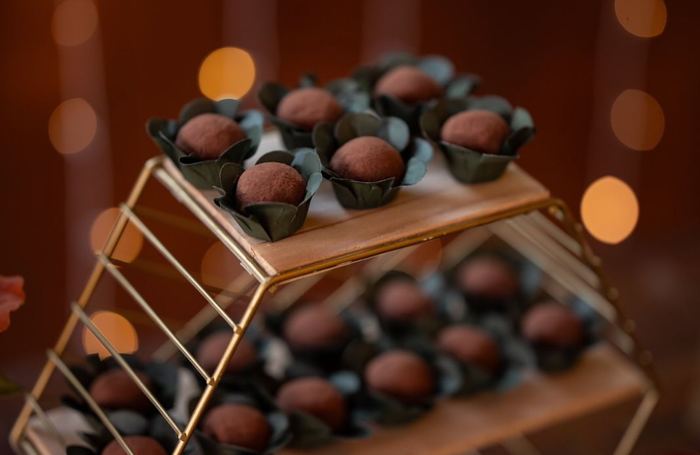 Brigadeiros trufados em forminhas verdes sobre suporte dourado, em mesa de festa iluminada