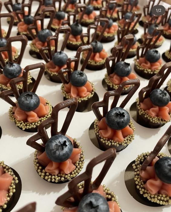 Doce autoral com base de chocolate, creme rosé, mirtilo, drageados dourados e escultura de chocolate