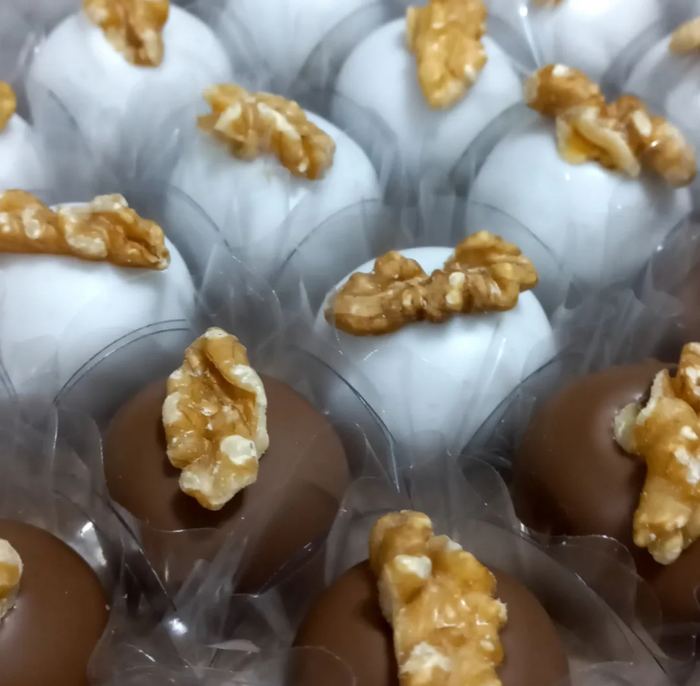 Doces de nozes banhados em chocolate branco e ao leite, com metade de noz no topo