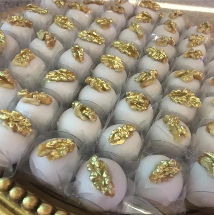 Doces brancos finalizados com nozes em dourado, dispostos em bandeja de prata trabalhada