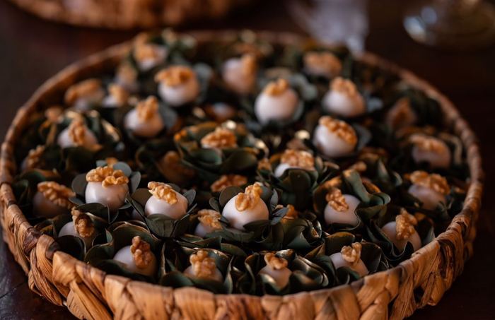 Doces de nozes em forminhas verdes escuras dispostos em cesta de palha