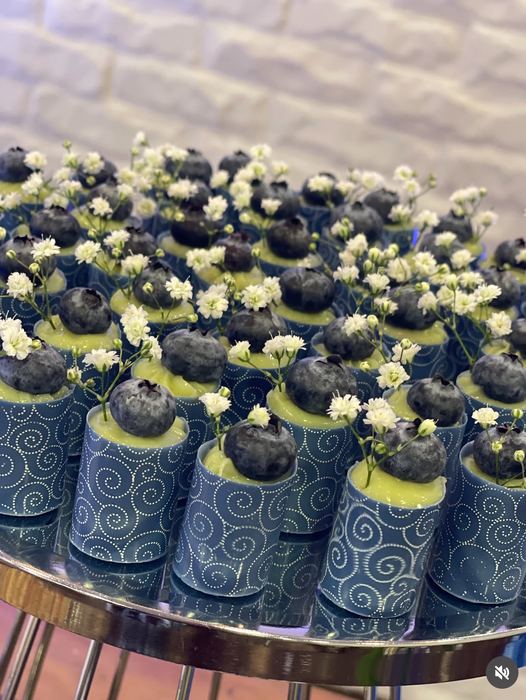 Copinhos de chocolate azul com creme, mirtilo e flores de gipsofila natural sobre bandeja espelhada