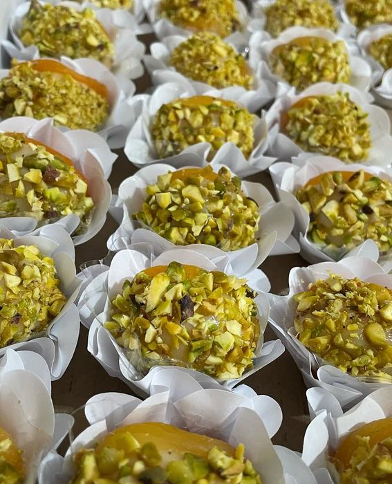Doces cobertos com pistache picado e damasco, em forminhas brancas de papel
