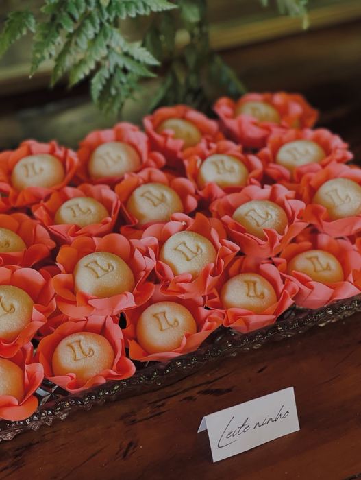 Doces de leite ninho com a inicial L aplicada em dourado, em forminhas coral, com plaquinha identificando o sabor