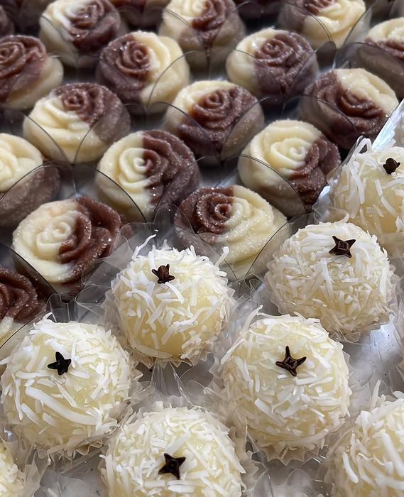Doces modelados em formato de rosa bicolor ao lado de beijinhos finalizados com cravo