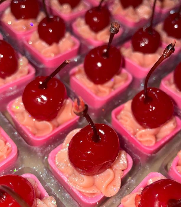 Doces em cápsula rosa com creme e cereja no topo, com brilho comestível